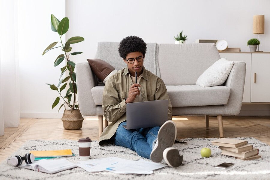 A student sitting on the floor with a laptop, studying and reviewing homeschooling materials.